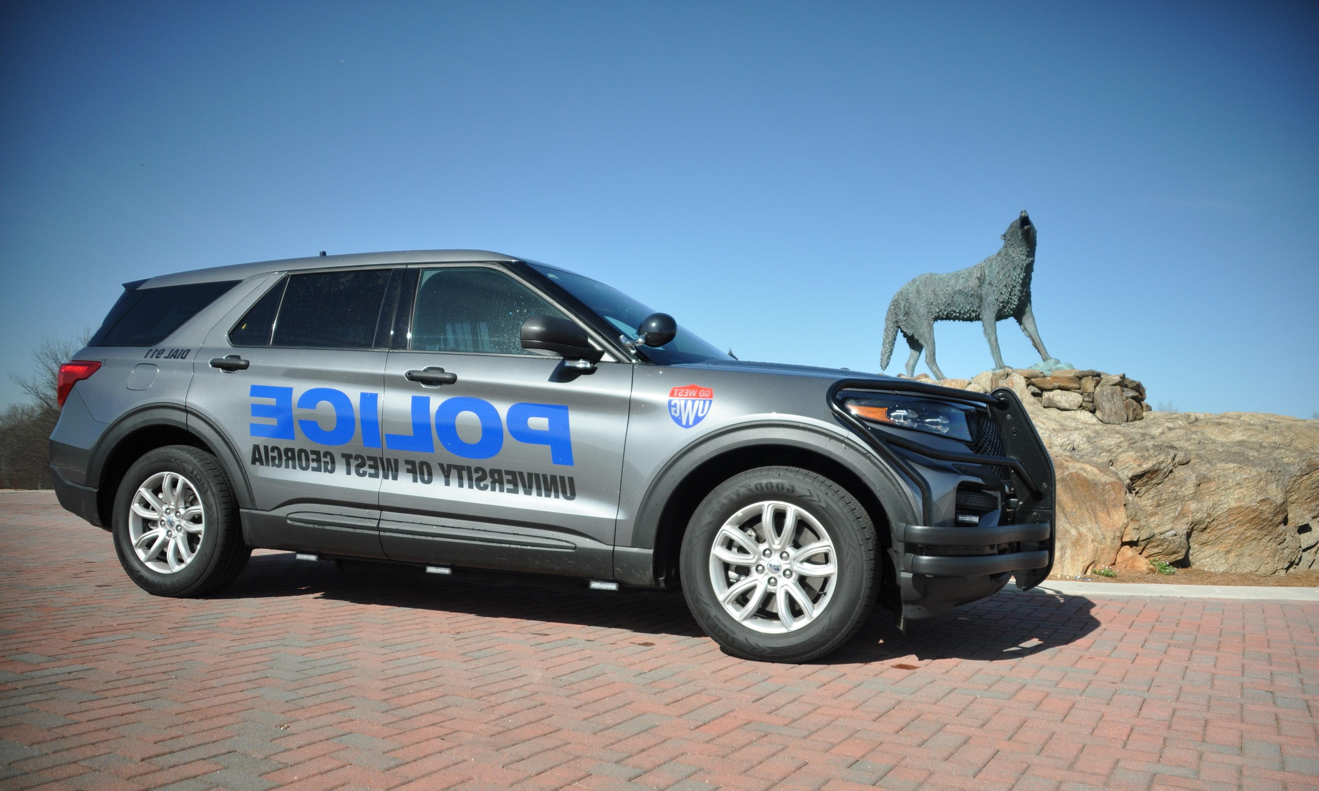 Dark grey police vehicle parked at wolf plaza with the wolf statue positioned behind.